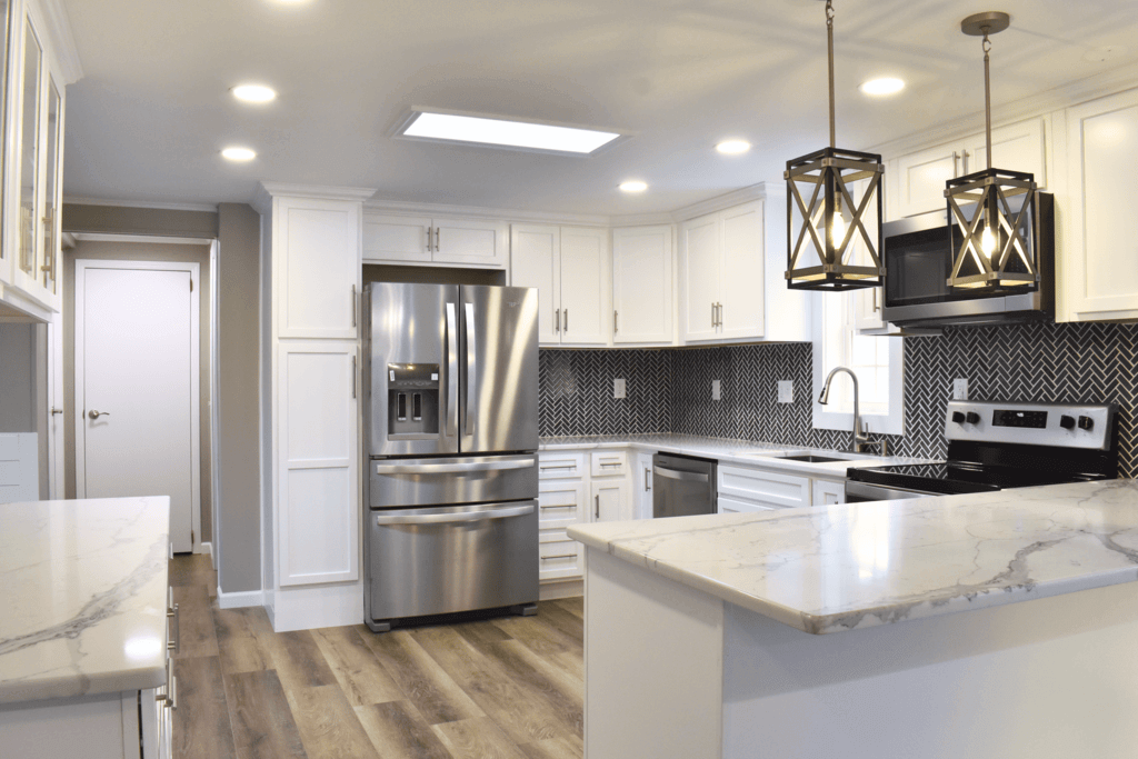 An expert kitchen remodel with white counters, white cabinets, a black and white backsplash, and new light fixtures.