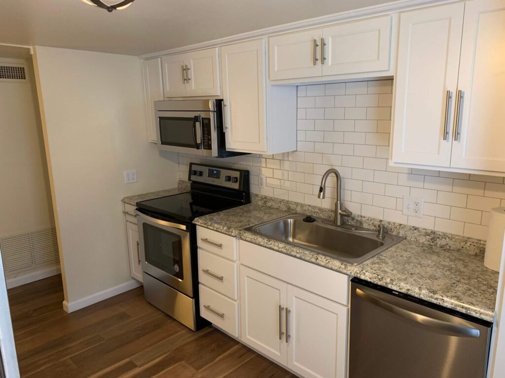 A kitchen remodel with white cabinets, a white backsplash, and granite counters.