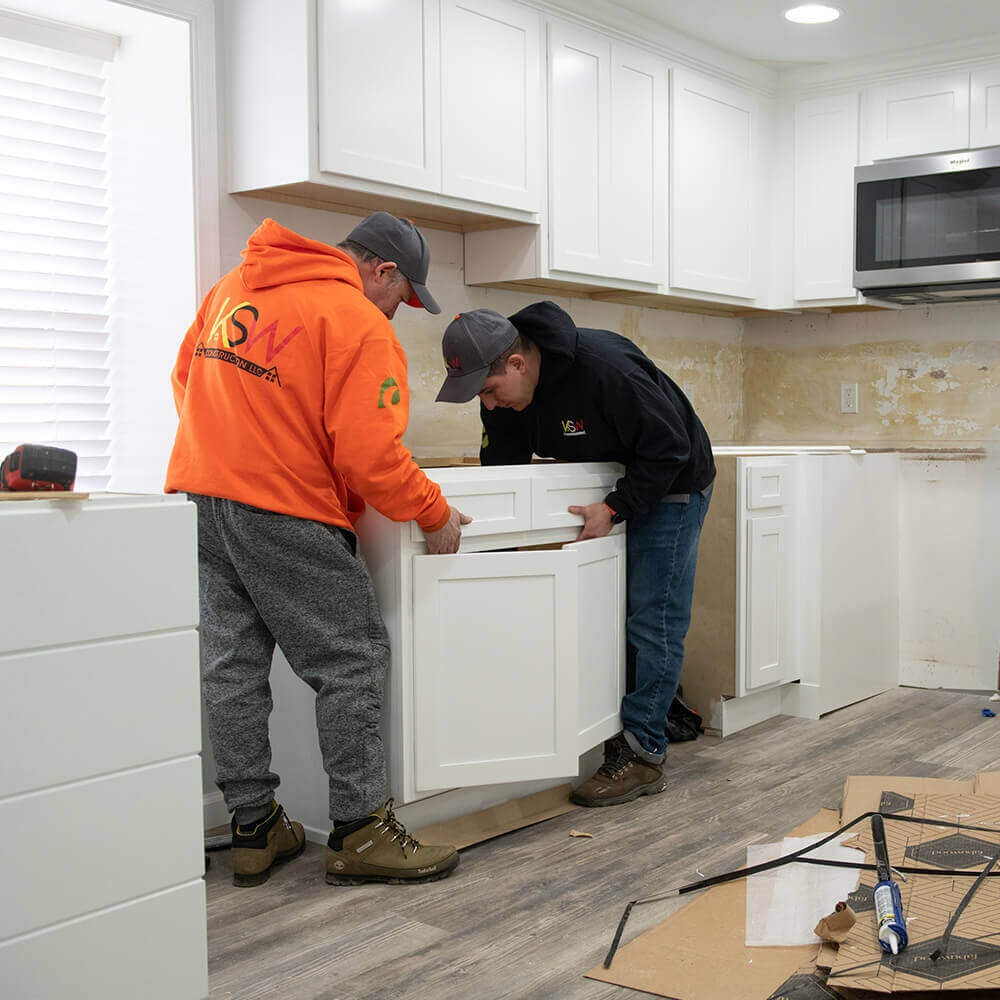 Two KSW Construction LLC crew members install cabinets into a kitchen remodel.